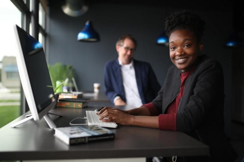 A payroll officer smiling at her desk while working on a computer.